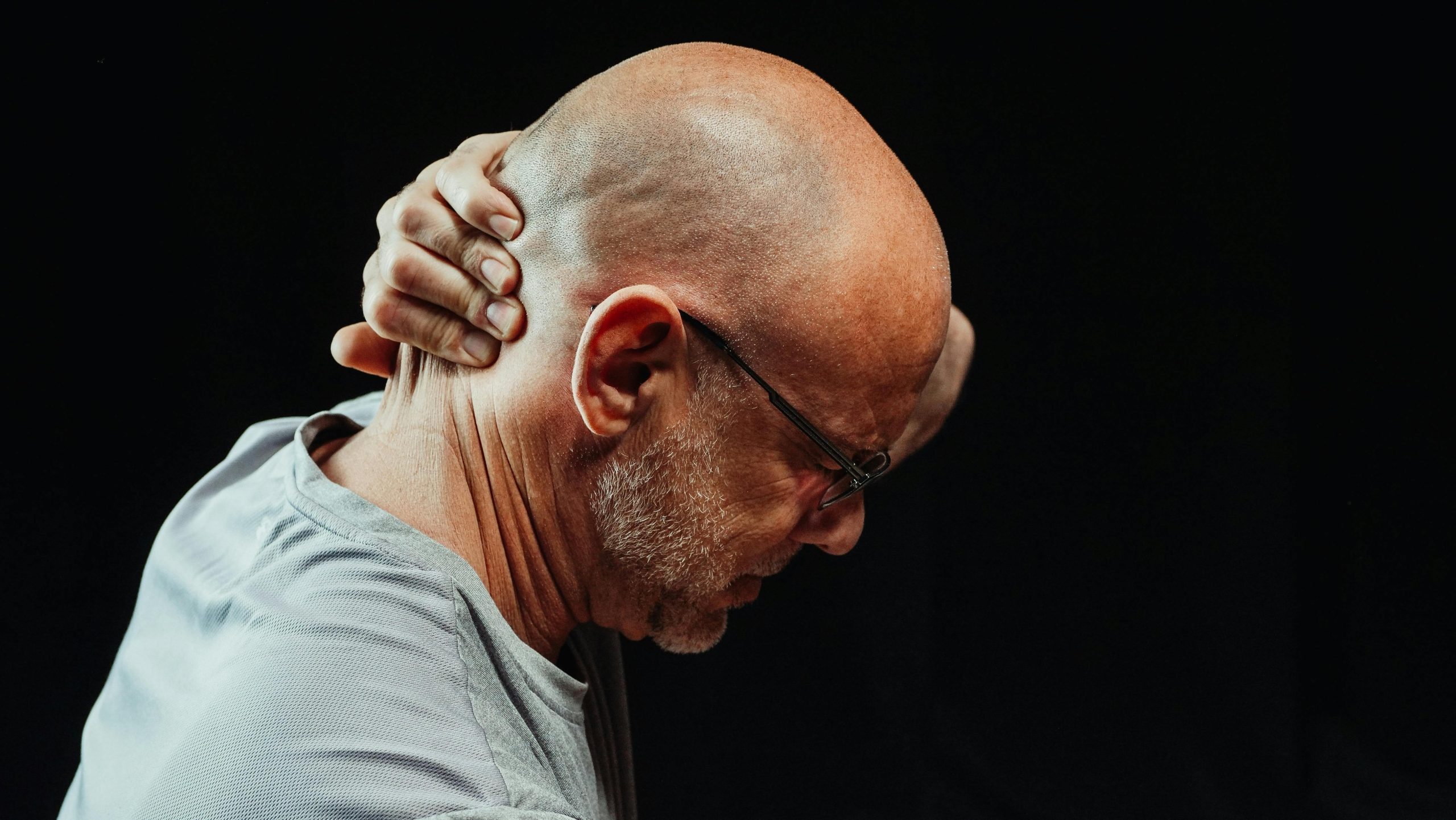 Side view of a man holding his neck in pain against a black background.